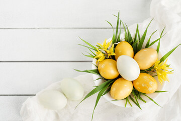 Easter yellow eggs and bright spring flowers with grass in a bowl on a white table background, top view, copy space. Festive decor, easter card