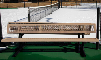 Empty tennis court bench with snow covering the court