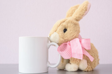 White coffee mug easter mockup and stuffed toy bunny with pink bow on lilac background