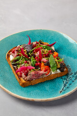 Bruschetta with roast beef, baked paprika and onion on blue ceramic plate. Toast with roast beef in contemporary style. Chef concept bruschetta in modern ceramic dishware. Handmade dinner plate.