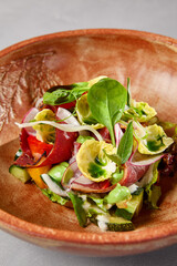 Salad with pastrami, vegetables and dressing on handmade ceramic bowl. Vegetables salad with roast beef in modern dishware on gray stone background. Contemporary food from chef. Handmade dinner plate.