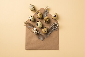Top view of big brown craft envelope cute feathers and small quail eggs with spots on it situated on beige isolated background copyspace