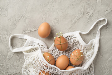 Top view photo of white string bag with brown eggs decorated by gypsophila flowers and twine on...