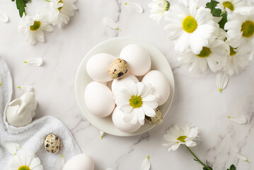 Top view photo of easter decorations festive table bouquet of chrysanthemum flowers ceramic easter bunny statuette towel and plate with white and quail eggs on isolated white marble texture background