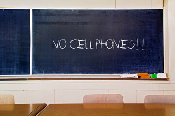 Very old scratched school board with "No Cell phones" written on it with chalk.