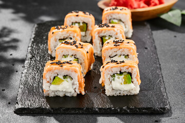 Maki sushi on dark slate. Hot philadelphia maki with baked salmon. Sushi roll with grilled salmon, cream cheese and avocado. Style concept japanese menu with black background, leaves and hard shadow.