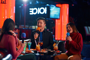 Asian friends having fun while singing karaoke on night party at the bar
