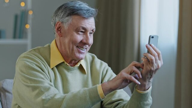 Happy elderly senior adult man holding phone make video call smiling grandfather looking at smartphone screen remote communicate use modern device positive old male speak on telephone share good news