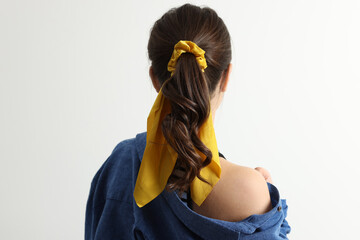 Young woman with stylish yellow bandana on light background, back view