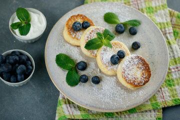 Cottage cheese pancakes with sour cream, raspberries, blueberries and mint, homemade traditional Ukrainian and Russian syrniki on rustic wooden background. Top view.