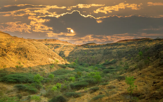 Sunset sky, sunlit clouds, old crumbling mountains and a dry river bed (wady). Subtropical winter. Deccan Plateau. India