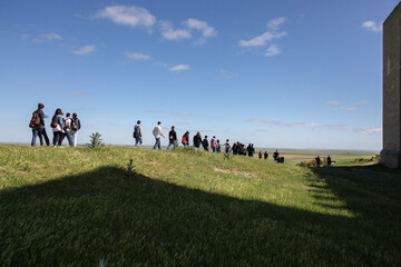 A group of people walking down a green hill near a medieval wall on a sunny spring day in a village of Spain 