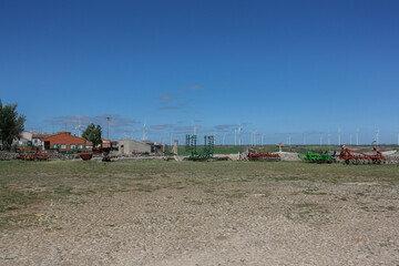 Fototapeta premium Wind turbines at the horizon over farm equipment on a sunny spring day