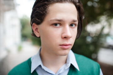 Obraz premium Teenage boy 17-18 year old with brunette hairstyle wear school uniform outdoors. Looking at camera. Hansome teenager kid. Generation Z.