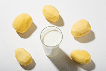 Potato milk alternative. A glass of milk and a raw potato on a white background.
