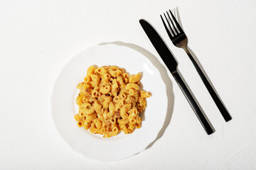 Curly Italian pasta with sauce on a white plate. Minimalism. White background. Pasta in cheese sauce. Knife and fork are black.