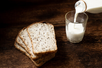 Pieces of bread with seeds and milk are poured into a glass. Dark wooden background. Morning breakfast. Healthy food.