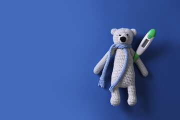 Toy bear with thermometer on blue background, top view. Space for text