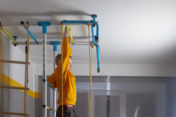 Fototapeta na wymiar The boy pulls himself up on the horizontal bar at the sports complex at home in the room