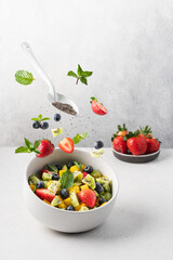Fruit salad of mango, kiwi, strawberries, blueberries and chia seeds in bowl. Concept food levitation, berries flight
