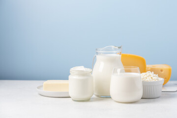 Milk, yogurt, cottage cheese, cheese, butter on light table and blue background. Side view of variety of dairy products