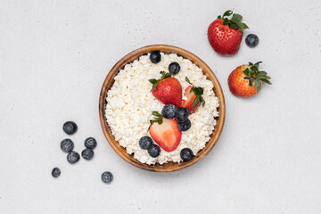 Cottage cheese in wooden bowl with berries on gray background. Dairy farm product