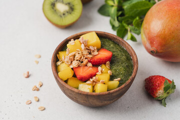 Kiwi smoothie wooden bowl with granola, mango and strawberries. Healthy vegan diet food concept