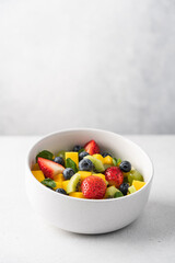 Pieces of mango, strawberries, blueberries, kiwi and mint in white bowl. Fruit fresh raw summer salad