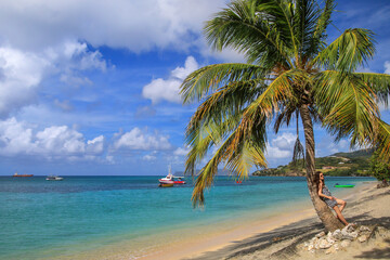 Young woman leaning on the palm tree at the beach, Hillsborough Bay, Carriacou Island, Grenada.