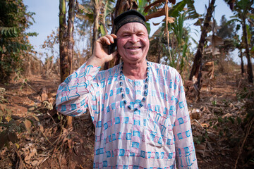 African albino senior makes a phone call and is happy. Man with albinism syndrome dressed in traditional African clothes. - obrazy, fototapety, plakaty