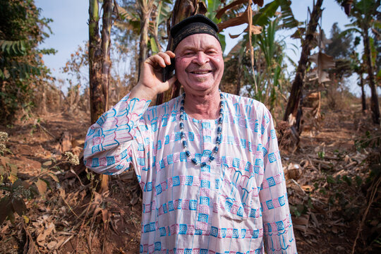 African albino senior makes a phone call and is happy. Man with albinism syndrome dressed in traditional African clothes.