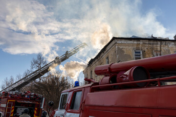 Firefighter works on boom of fire engine. Fireman on sky background. Burning old building in the historic center