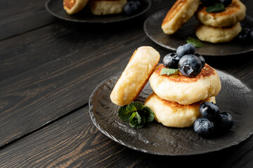 Cottage cheese fritters with blueberries on dark wooden background with copy space
