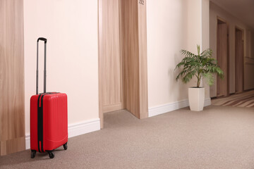 Modern red suitcase in empty hotel corridor