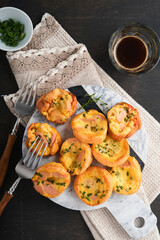 Delicious egg muffins with green onions, bacon, cheese and tomatoes on wooden board on old wooden rustic background. Healthy high protein and low carb breakfast. Homemade food.