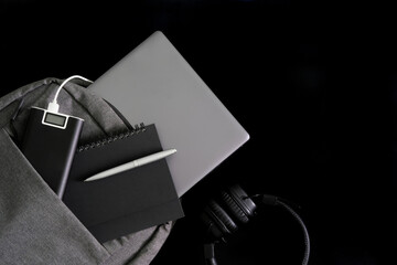 Silvery laptop lies in gray backpack with notepad, pen and external battery - power bank, next to...