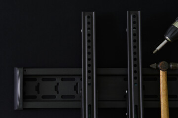 odern metal bracket for wall mounting TV or computer monitor on a black background, next to a hammer and an electronic screwdriver