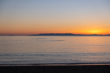 Sandy beach at sunset. Greece. Calm sea water, small ripple, orange color sky.