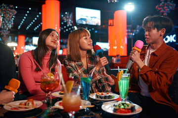 Group of asian guys and girls singing songs at karaoke club