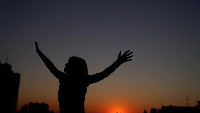 Silhouette female dancing and feeling happy outdoor at sunset with urban background. Woman pumping his fists in the air, victory businesswoman concept, dancing, raising hands and waving. 4k video