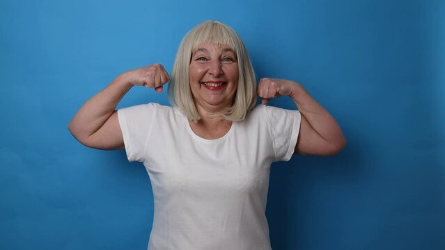 Healthy mature senior 50s woman showing arms with plaster after vaccine, celebrating a victory over bright blue color background