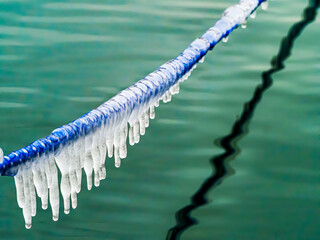  Close-up of a icy mooring rope with reflection in green colored water surface.