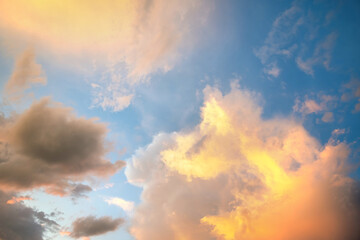 Dramatic sunset sky landscape with puffy clouds lit by orange setting sun and blue heavens.