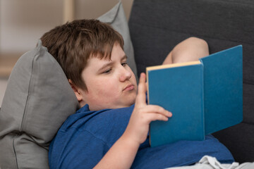 A reclining young boy reads his school reading at home.