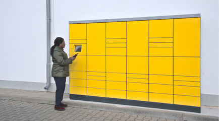 Automated Post package station with woman at the control screen holding mobile phone 