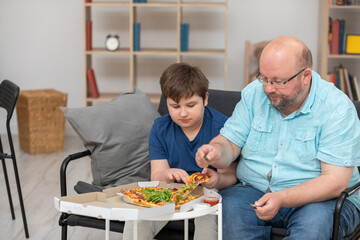 A father and son are sitting on the sofa sharing slices of pizza.