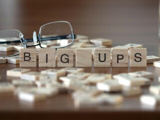 big ups word or concept represented by wooden letter tiles on a wooden table with glasses and a book