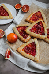 Bright and tasty galettes with blood oranges. Open mini pies with citrus fruits on parchment paper. Flat lay with sweet pastries