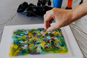 Drawing art process painting with alcohol ink on liquid epoxy resin Petri Dish Art . The caucasian female hand with a wooden stick makes a drawing on the surface. Bright colors. Beautiful patterns.