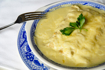 Swiss enchiladas, plate of Swiss enchiladas with Manchego cheese and green sauce on a table with cutlery ready to eat, Mexican food, close up view
